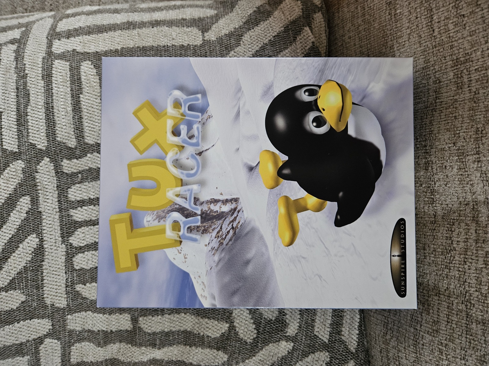 the physical copy of the 2000s game tux racer from the front, showing box art of tux racing on his stomach with the game's logo above him